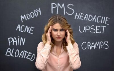 woman holding head with words pms moody headache acne pain bloat cramps